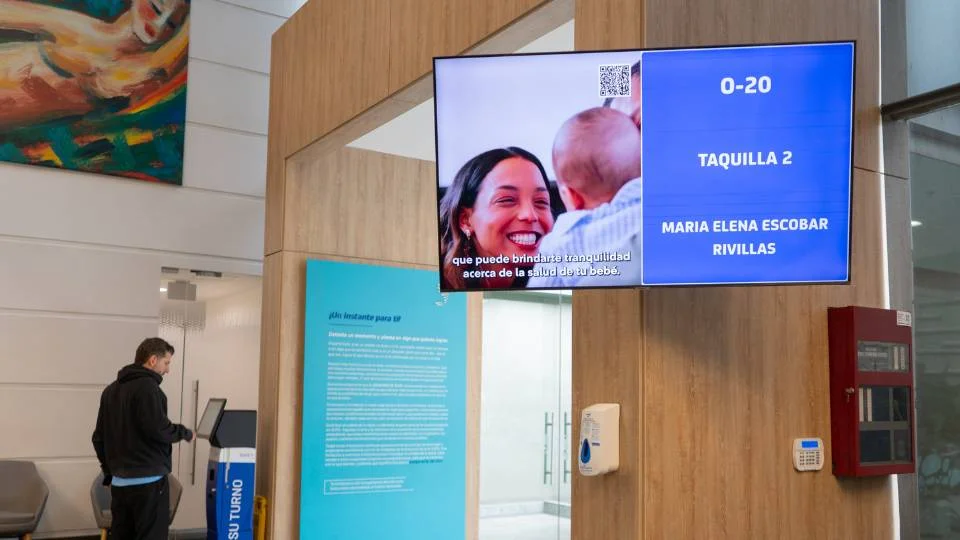 Pantalla de llamado de turnos combinada con cartelería digital reproduciendo video corporativo en sala de espera